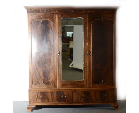 A stained wood triple wardrobe, pendented cornice piece, centre mirrored panel door, two drawers under, ogee bracket feet, wi