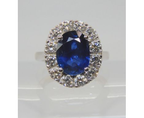 A SAPPHIRE AND DIAMOND CLUSTER RING set throughout in 18ct white gold, set with an oval mixed cut sapphire of estimated appro