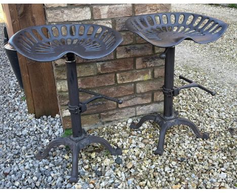 Two cast iron tractor seat stools with adjustable swivel tops.