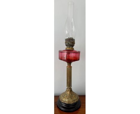A 19thC cranberry and brass oil lamp with black ceramic base. 48cm h to fitting.