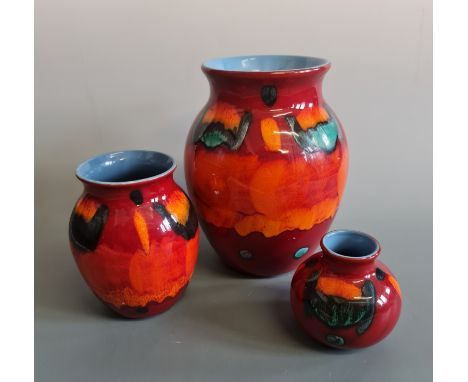 Three Poole Pottery vases in graduated sizes, orange, green and blue pattern on red background with blue interiors, heights a