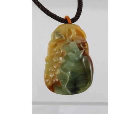 AN ORIENTAL CARVED BI-COLOUR JADE PENDANT on a plaited cord, 40cm long 