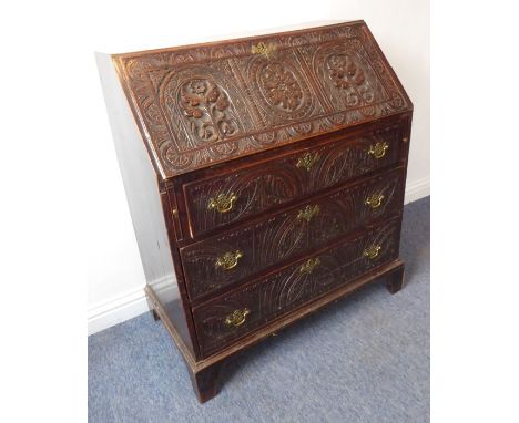 A late 18th century oak writing bureau; later carved with large lunettes and flowerhead designs in the 19th century manner, t