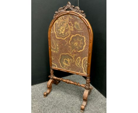 A Victorian walnut carved firescreen, arched floral crest, inset with floral needlework panel in tones of cream, plum and bro