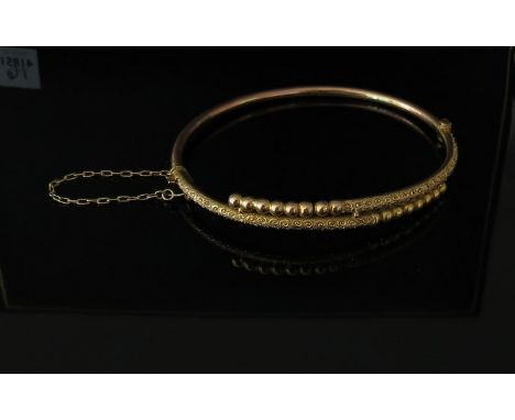 A gold stiff hinge bangle with engraved and ball design stamped 9ct, 4.7g