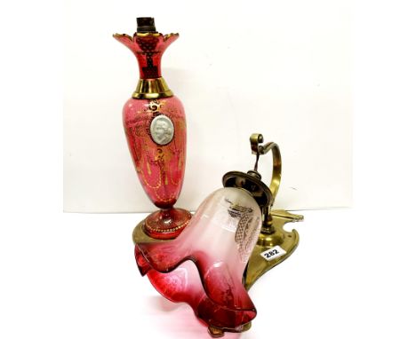 An Art Nouveau brass wall light with frosted cranberry shade, H. 34cm. Together with a gilt cranberry glass table lamp, H. 35