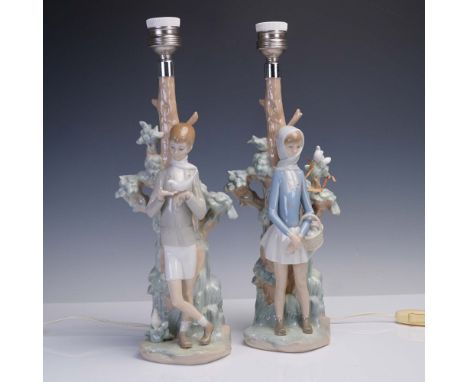 A charming pair of porcelain table lamps by Lladro, each featuring a young figure posed beside a stylized tree. The girl (mod
