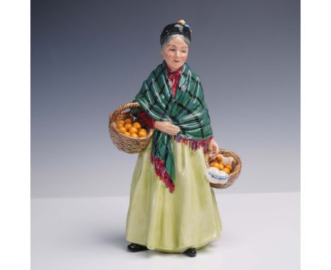 This hand-painted figure depicts an elderly woman in a green tartan shawl and yellow skirt, carrying two wicker baskets fille