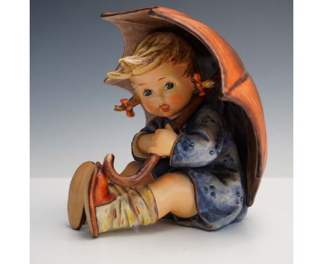 This charming large Goebel Hummel figurine features a young girl seated under an oversized umbrella, dressed in a blue coat a