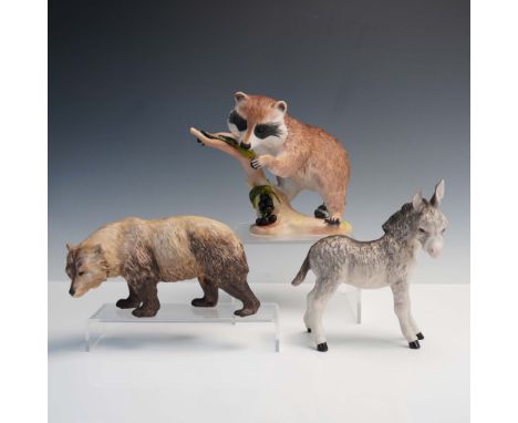 Set of three hand-painted porcelain animal figurines by Cybis, depicting a raccoon perched on a grapevine branch, a brown bea