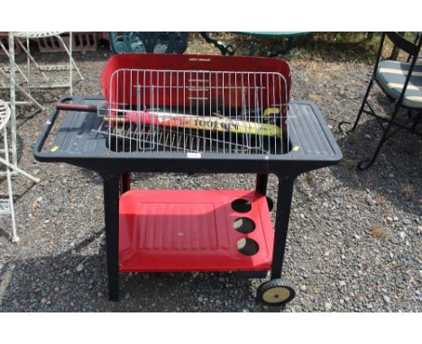 A wheeled metal bbq with tools etc