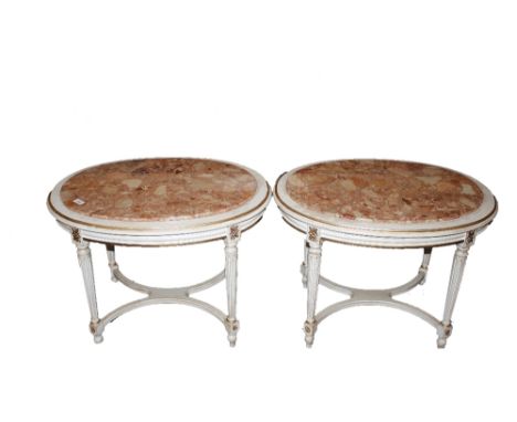 A pair of oval cream and gilt decorated lamp tables with marble inset tops, raised on turned tapering reeded supports united 