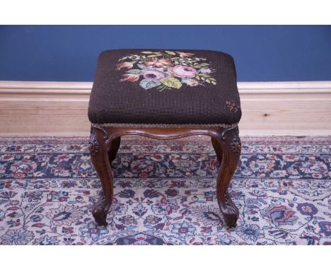 A Victorian carved walnut framed footstool with tapestry top on carved cabriole supports.