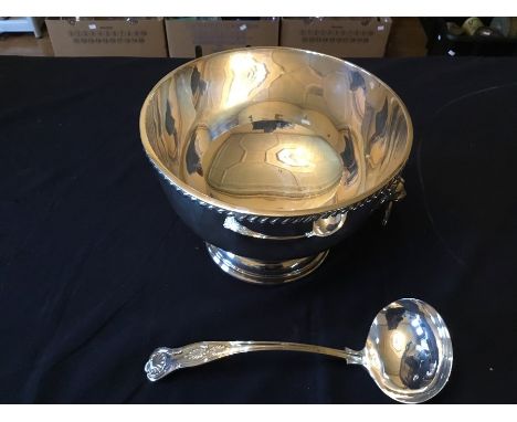 A plated punch bowl with lion mask loop handles and large ladle spoon.