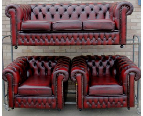 A maroon leather three seat Chesterfield sofa, with buttoned upholstery, and two matching chairs, each piece with metal butto