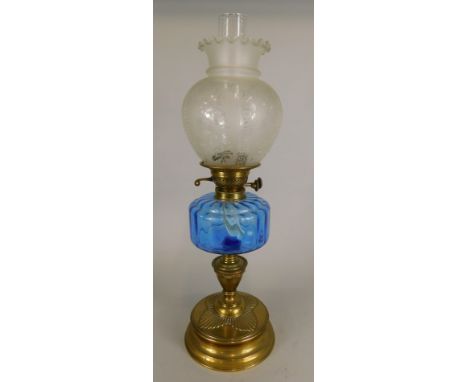 An early 20thC brass oil lamp with double burner, clear blue glass reservoir, acid etched shade and glass chimney, the base 3