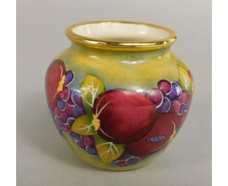 A Moorcroft enamel small vase, decorated with a band of fruit on a green ground, signed to underside J.E.H., 5cm high