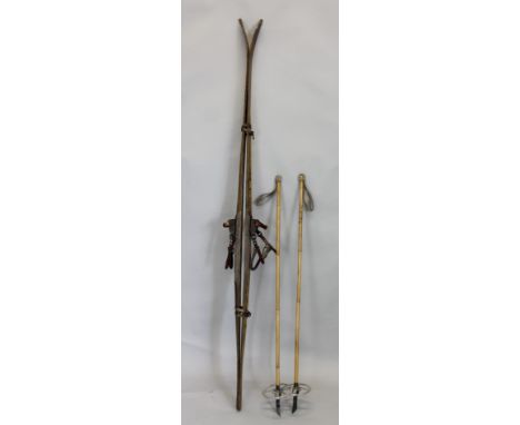 A pair of vintage ash skis, with leather fittings and part bamboo poles.