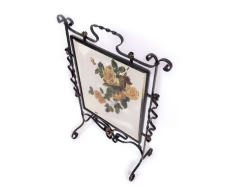 A wrought iron framed firescreen, in black with central mirror, partially painted with roses, with a central twist handle, on