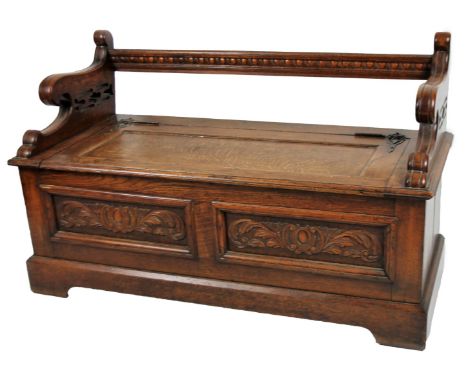 A late 19thC oak monk's bench, with compressed horizontal bar back, scroll arms and log box seat, fronted by two carved panel