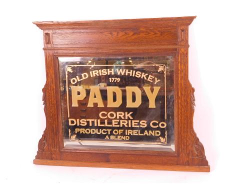 An Edwardian oak over mantel mirror, centred by an Old Irish Whiskey Paddy Cork Distilleries glass advertising panel centre, 