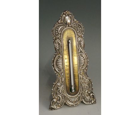 A late Victorian silver mounted desk thermometer, the front silver panel chased and embossed with scrolling design, vacant ov