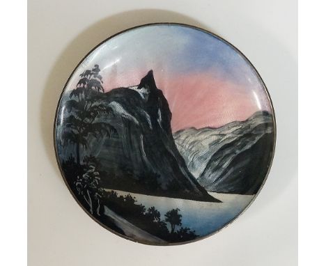 A circular enamelled silver dish the engine turned ground enamelled with stylised mountains, lake and trees with pink setting