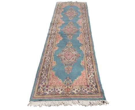 A good Kirman runner, three floral diamond shaped medallions on light blue ground, conforming spandrels and floral guard stri