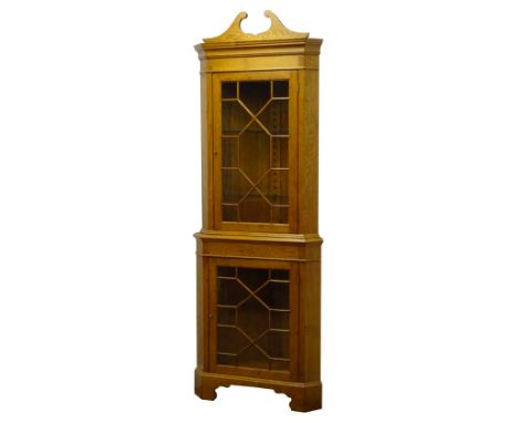 Graduated pair of 20th century golden oak standing corner cabinets, swan neck pediments and astragal glazed doors, on shaped 
