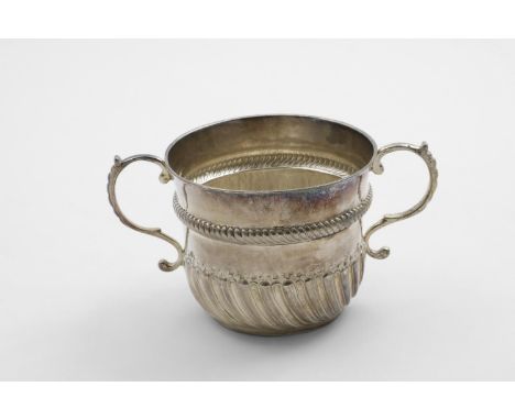 A WILLIAM III PORRINGER with twin s-scroll handles and a campana-shaped bowl with embossed part fluting and a moulded ropewor