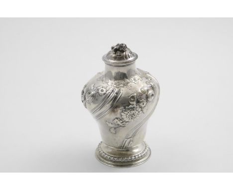 AN EARLY GEORGE III TEA CADDY of vase form, decorated with wrythen fluting and repousse floral  garlands, resting on a gadroo