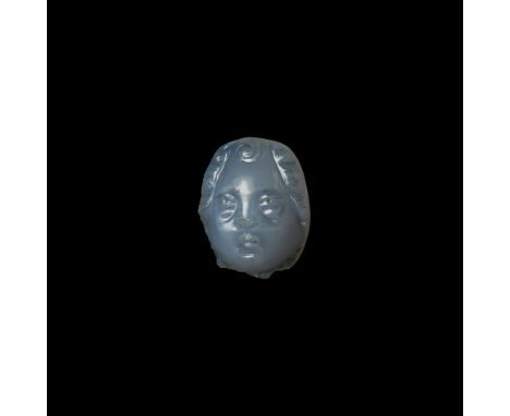 3rd century AD. A carved chalcedony phalera formed as a head with lentoid eyes, small pursed lips, full cheeks, fleshy chin a