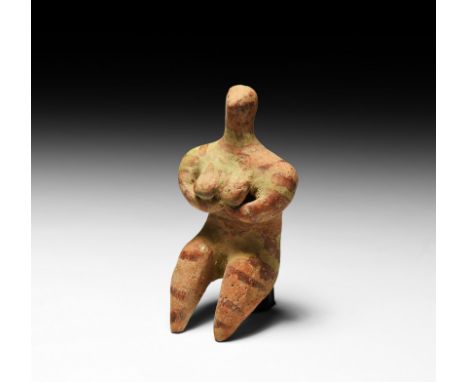 6th millennium BC. A ceramic figure modelled as a nude female, seated, knees drawn up to chest, arms held to body, hands cupp