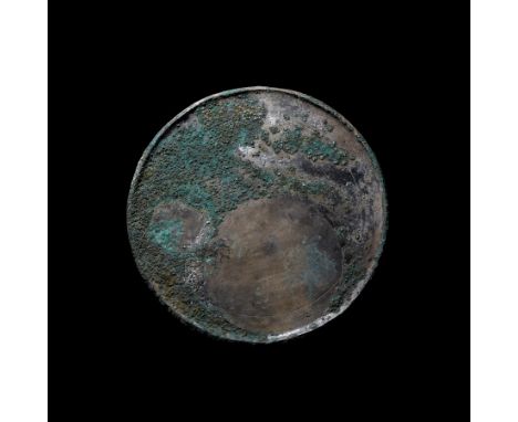 1st-2nd century AD. A solid bronze mirror comprising a wide disc with a folded edge; traces of the wooden mounting platform t