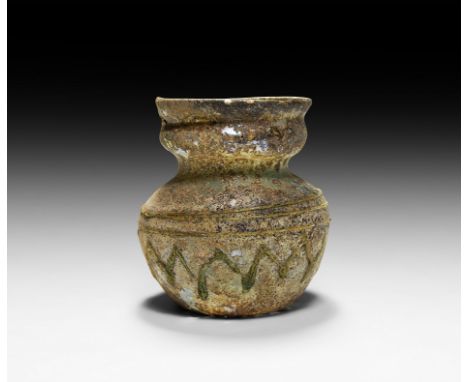 3rd-4th century AD. A glass storage vessel with carinated body, rounded shoulder, short neck and waisted rim, decorated with 