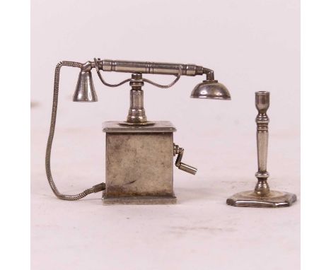 A miniature silver model of a vintage telephone, h.4cm; together with a miniature silver table candlestick, h.3.5cm, gross we
