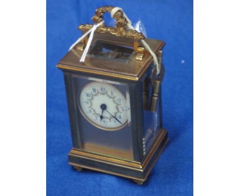 French gilt brass carriage clock with circular enamelled face and foliate wreath swing handle.