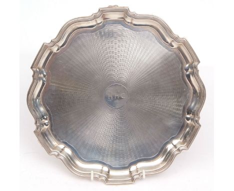 George VI salver of shaped circular form with engine turned centre and initialled cartouche and raised on three cast and appl
