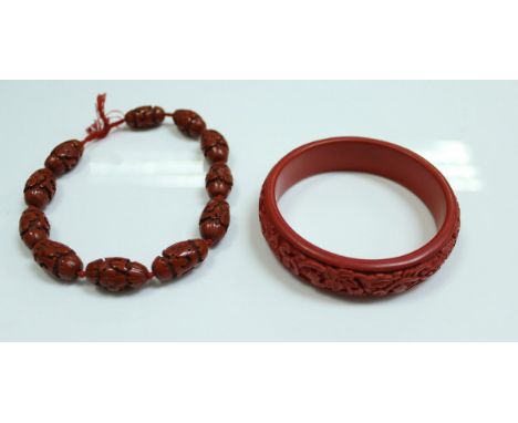 A cinnabar lacquered bead necklace, each bead approx 2 cm long, together with a similar bangle, internal diameter 6.5 cm and 