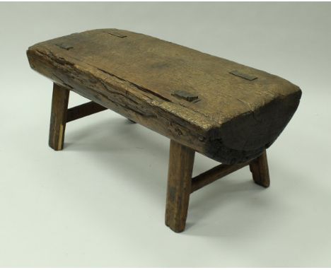 An Indonesian pig bench of half cut trunk form, raised on splayed supports, 136 cm wide