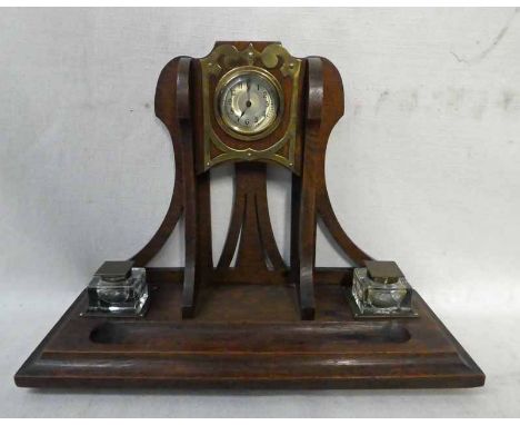 An Arts and Crafts oak Desk Stand, vertical bracket, pierced and set centrally with a clock, moulded edge rectangular base wi