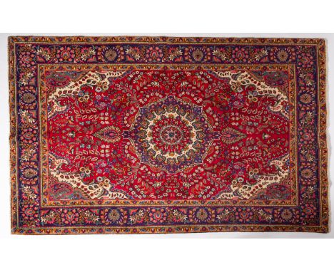 A Tabriz carpet, the madder cartouche field with a central indigo, ivory and red palmette pole medallion, all over floral fol