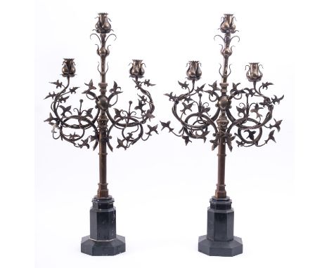 A pair of metal three light candelabra in Gothic taste, circa 1900; each with a central raised socket above two others on scr