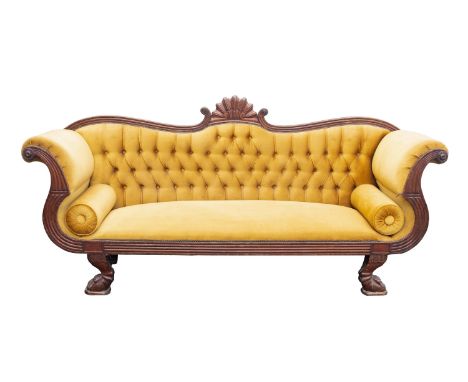 A Regency carved mahogany and upholstered sofa, early 19th century; the serpentine toprail of the buttoned backrest with roca