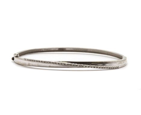 A 9ct white gold diamond bangle, with a crossover row of eight cut diamonds claw set to the upper half, to plain lower half, 