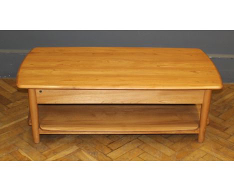 An Ercol blond elm coffee table, the rising cantilever top over a concealed tray, raised on turned supports, united by undert
