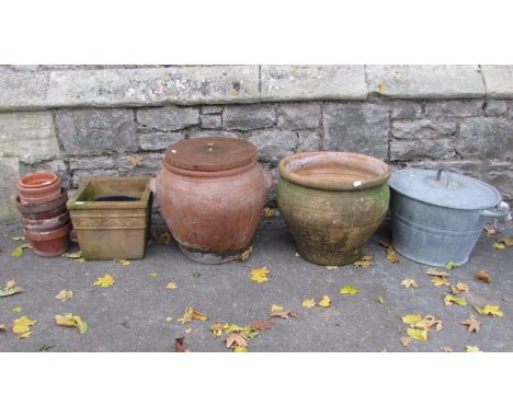 A weathered terracotta crock with moulded handles, incised band and loose lid, together with further terracotta pots and a ga