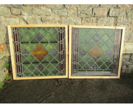 A pair of reclaimed stained glass window panels with foliate detail, mounted in later simple pine frames, 70 cm square (overa