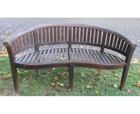 A stained and weathered  teak banana shaped garden bench, 159 cm long