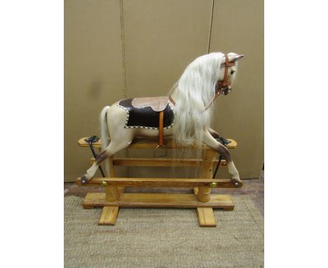 A traditional rocking horse with painted finish, raised on a pine frame with central supports, leather harness, etc, restored